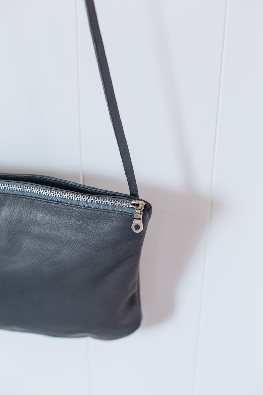 Close up of grey leather crossbody bag with a silver zipper on a white background