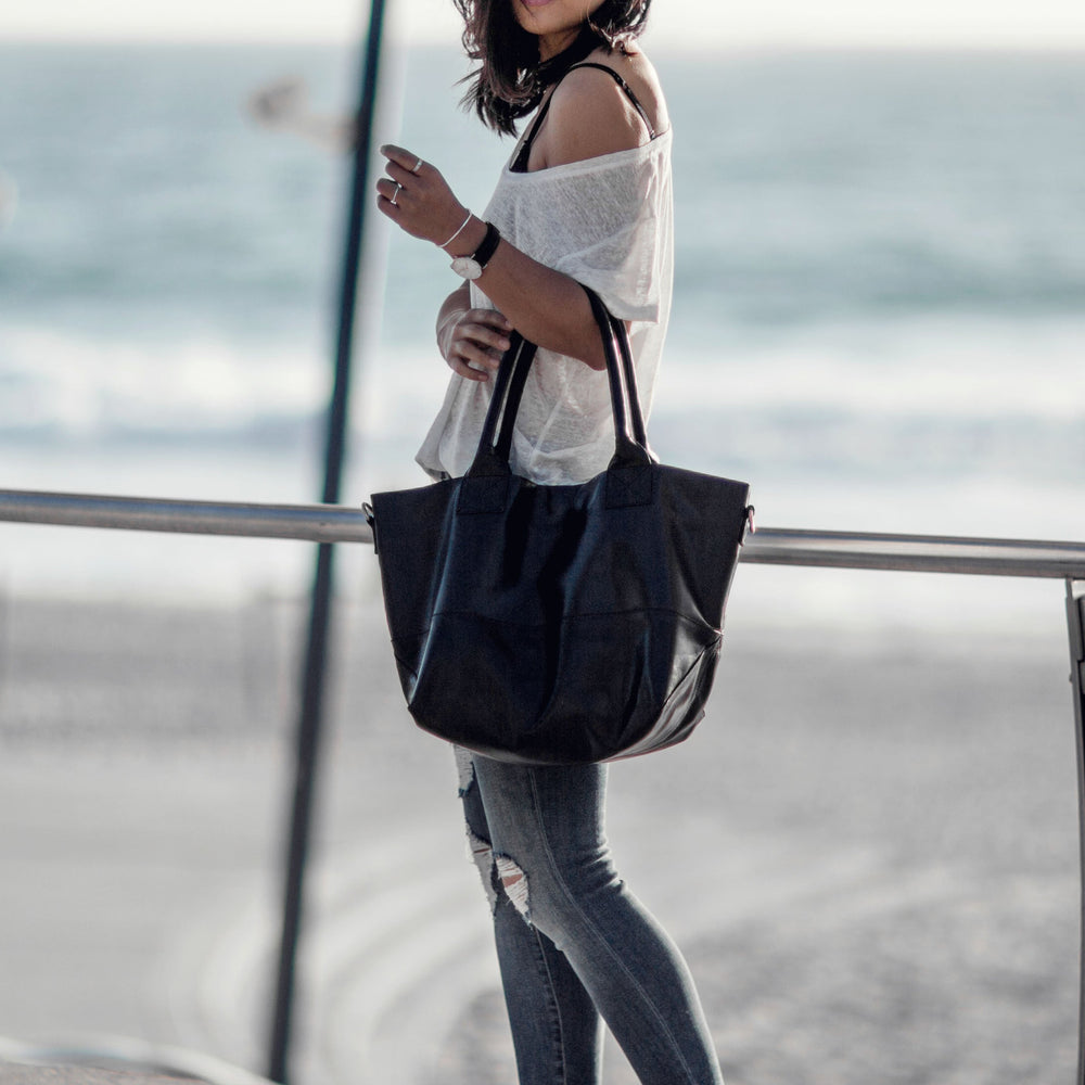 Woman holding a black tote bag by the beach