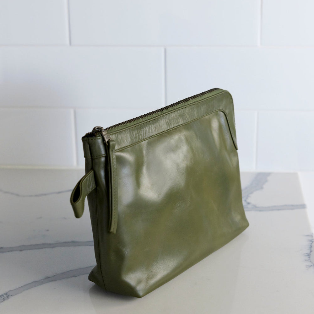 A green, solid-colored Sicily toiletry bag placed on a surface, with a simple and elegant design.
