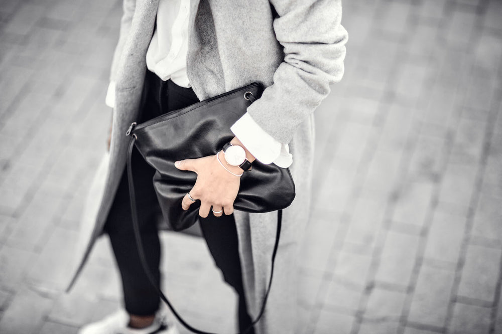 Woman in black jeans with grey coat holding a black bag with strap haging down