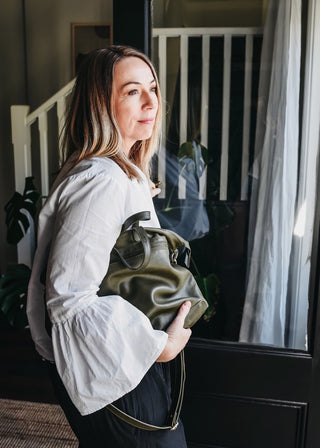 Woman looking out open door with Army Rome Lether TOte under under showing how supple the leather is.