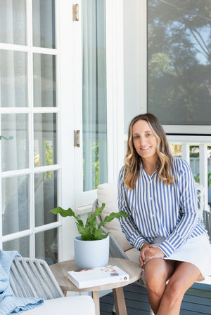 Owner of Australian leather handbag brand, Bahru Leather. Wearing a striped blue and white shirt sitting outside and smiling at the camera