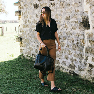 Woman holding a black leather tote 
handbag against a stone wall