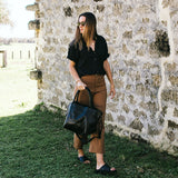 Woman holding a black leather tote 
handbag against a stone wall