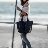 Woman holding a black tote bag by the beach