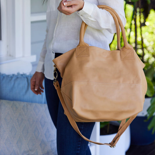 A woman wearing a white shirt carrying a nude-coloured leather tote bag with an adjustable strap.